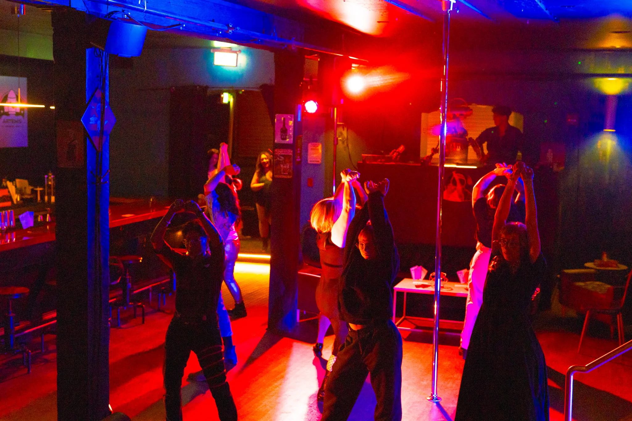 Dancers moving together on the floor at Artemis under red and blue light, arms raised overhead