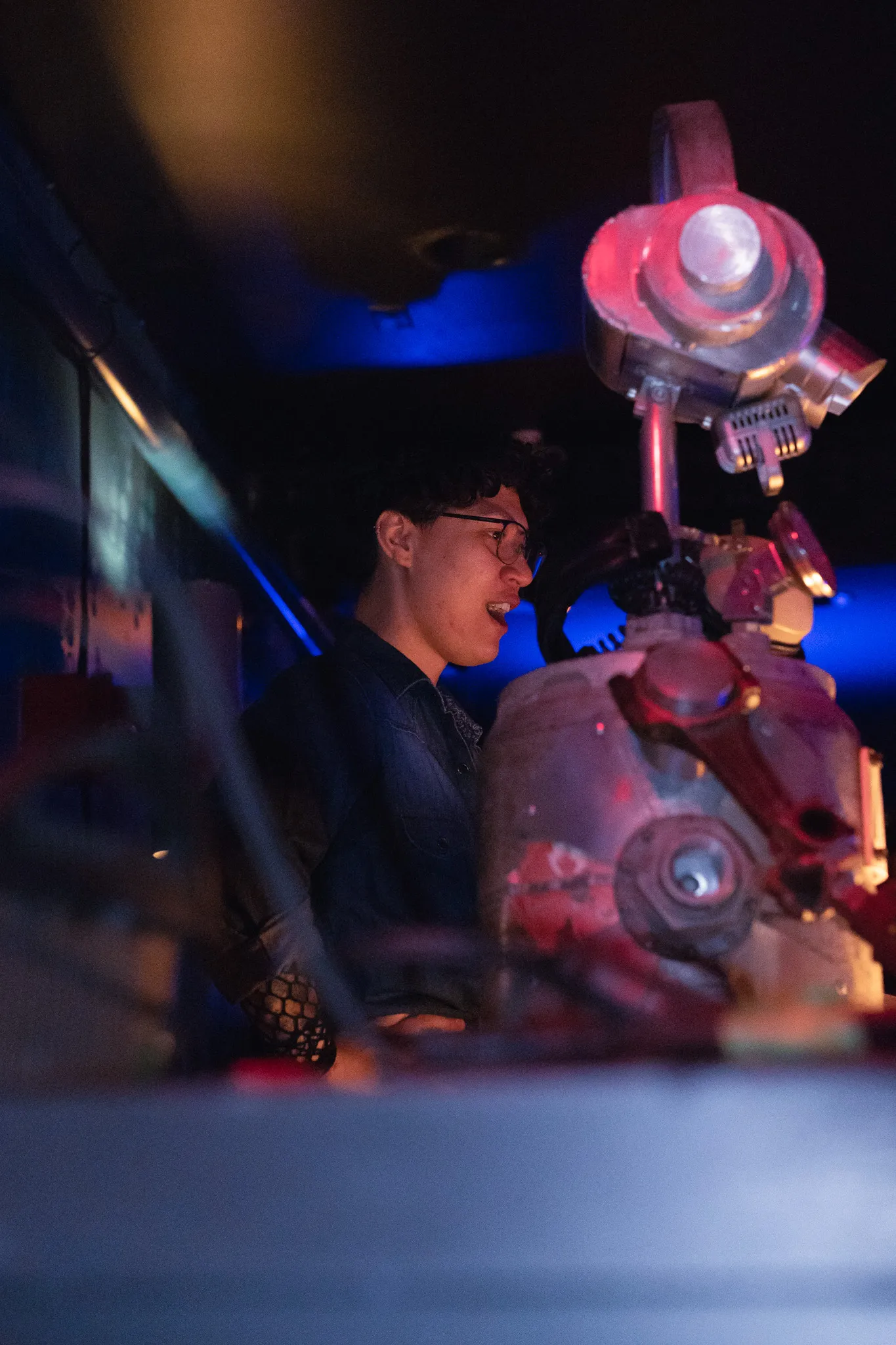 The lighting operator at the board in the dark, lit red and blue, watching the stage